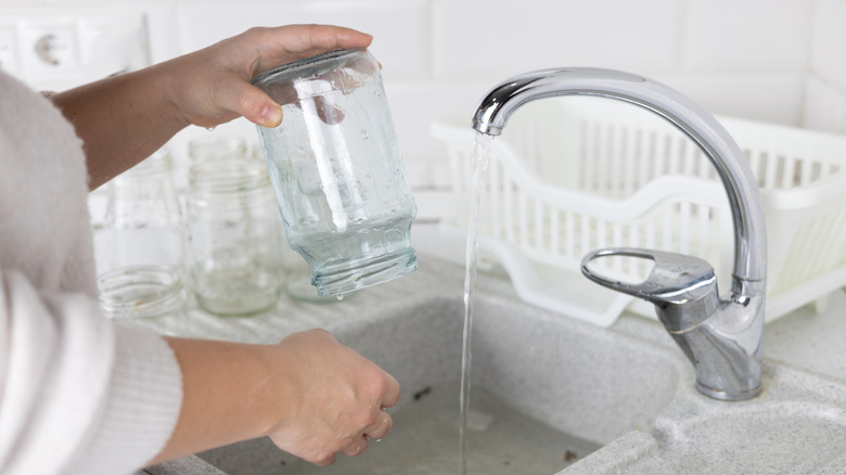A person cleans a large mason jar in the kitchen sink.