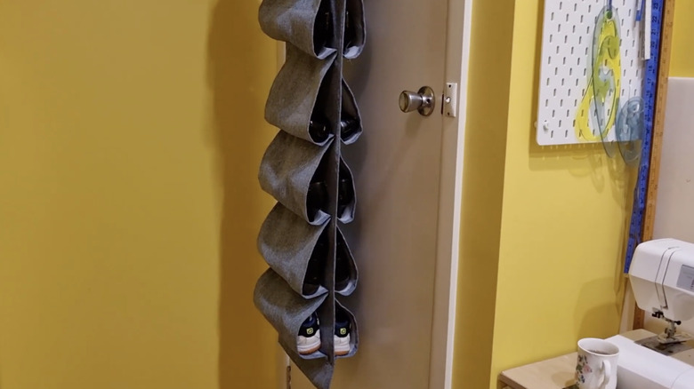 A gray fabric shoe organizer hangs behind a door in a craft room with yellow painted walls.