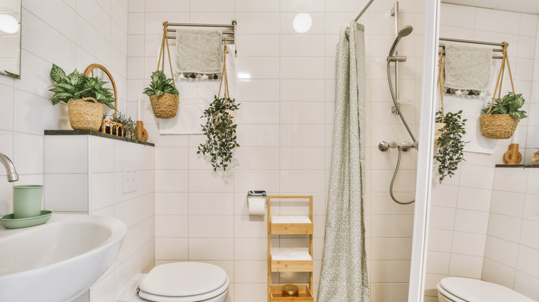 A bathroom with plants, wicker baskets, and a wooden shelf next to a green shower curtain.