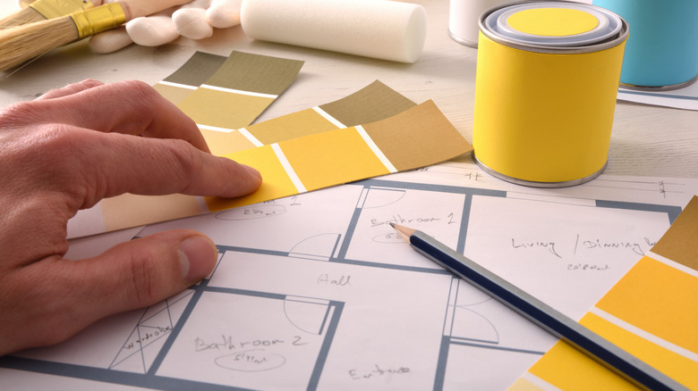 Hand holding yellow paint swatches on top of home design blueprints.
