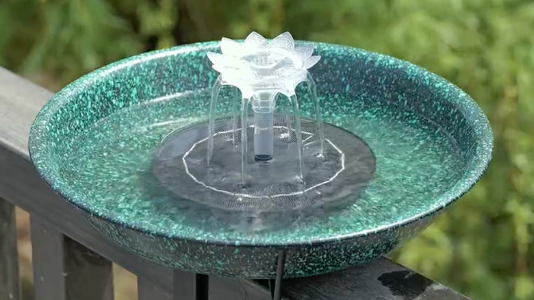 A turquoise bird bath with a fountain feature mounted to a wooden deck railing