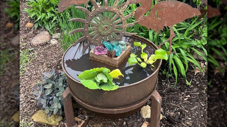 A copper apple butter kettle filled with water, pond plants, and decorations to be used as a bird bath