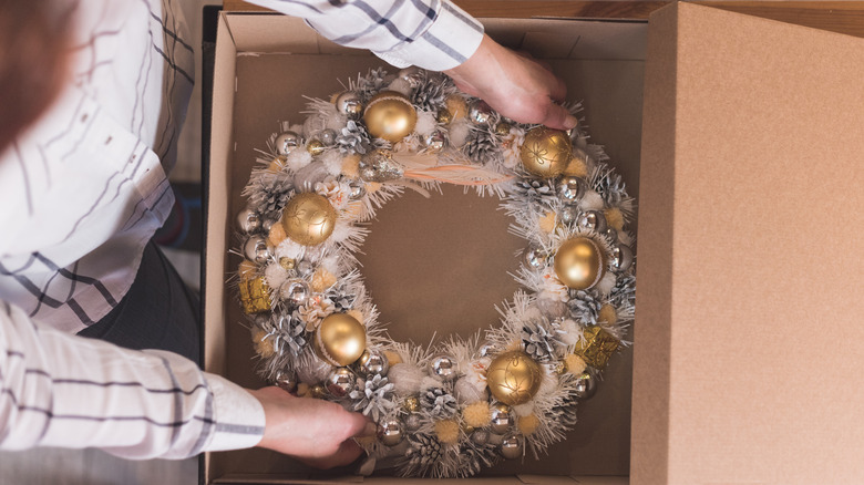 A person puts a wreath decorated with ornaments away in a storage box
