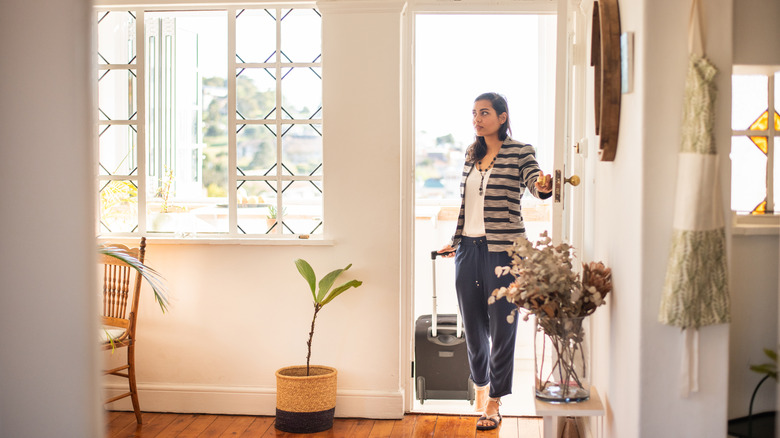 Woman entering a home with a suitcase in tow