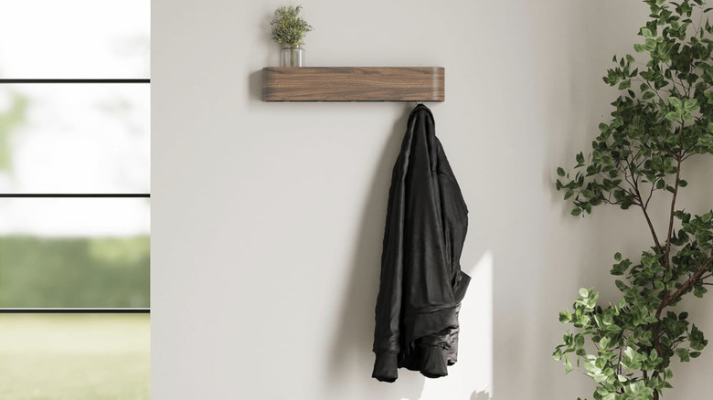 Kazai coat rack on a white wall with a black jacket hanging and two plants
