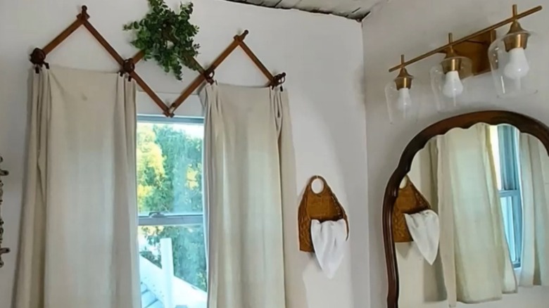 White curtains hang in bathroom above window from a wooden accordion rack.
