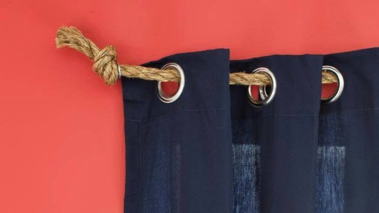 Dark blue curtains hung up with jute rope and eyebolts on a bright orange wall.