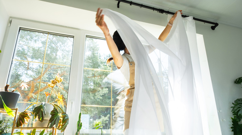 Woman removing curtain from traditional metal curtain rod.
