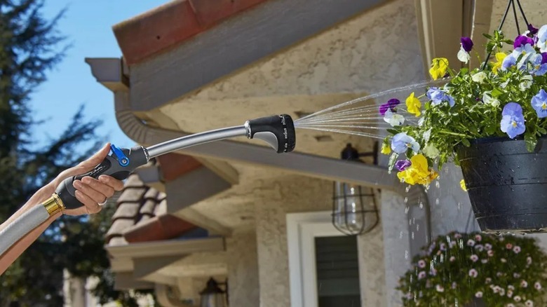 Person watering hanging basket of flowers using the Niagara Multipattern Watering Wand from Harbor Freight.