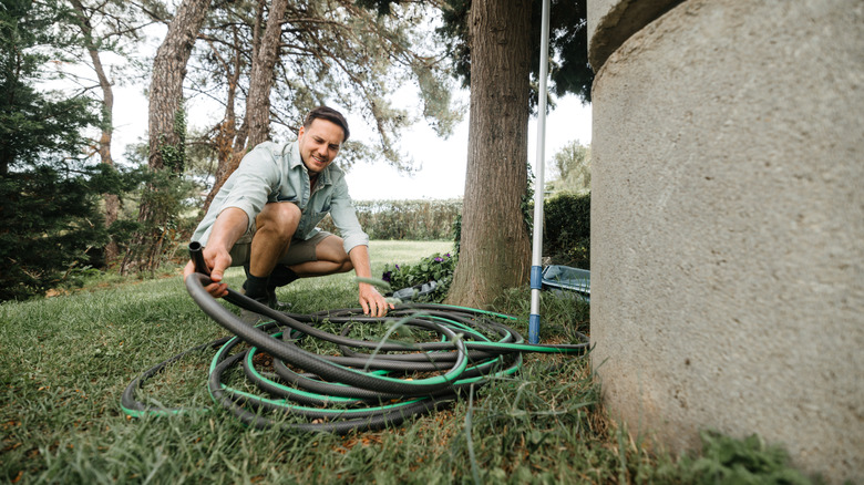 Person trying to gather long hose in yard