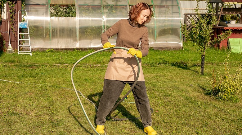 Person in backyard pulling a garden hose across the lawn