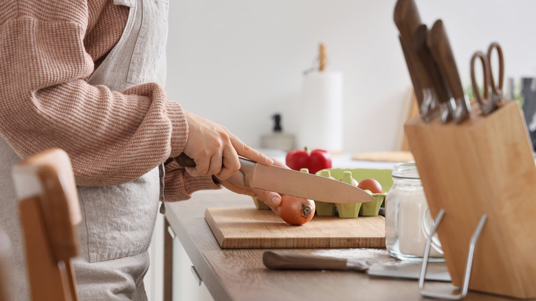 Woman cutting vegetables with a large knife block in the corner