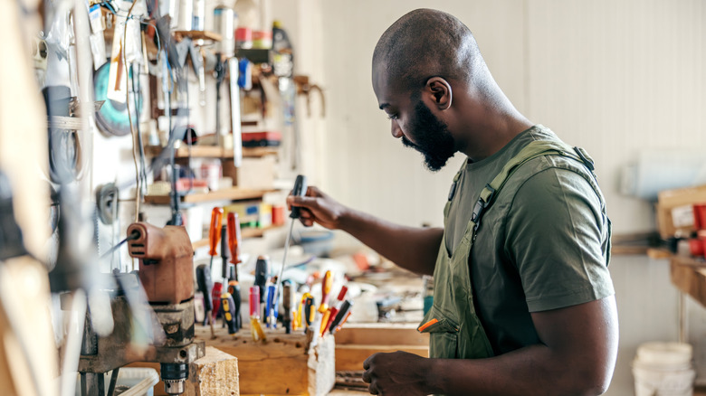 Man getting screwdriver from tabletop tool storage.