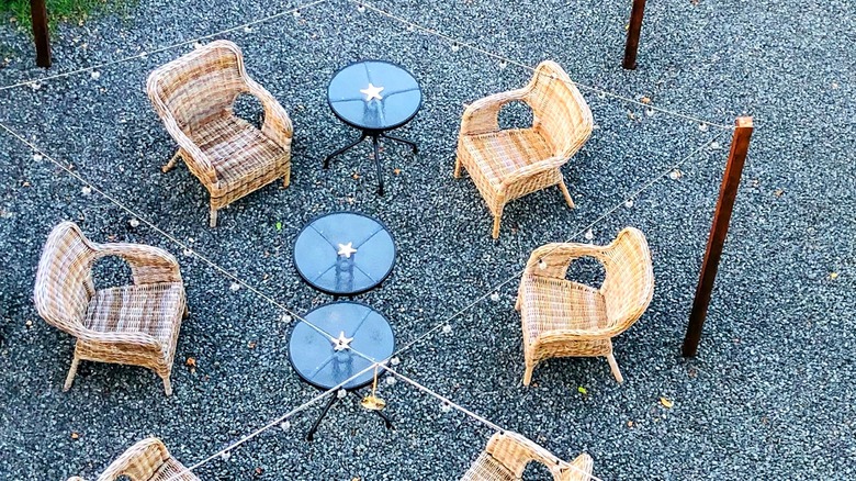 An outdoor space featuring chairs and small tables on gravel with string lights above