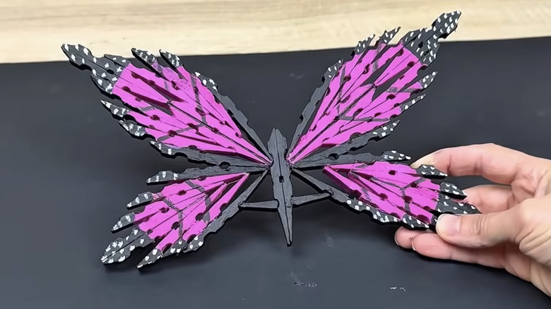 A hand holds a painted purple butterfly made out of wooden clothespins.