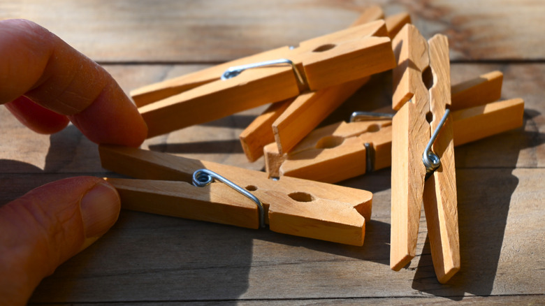 A hand reaches for wooden clothespins on a wooden tabletop.