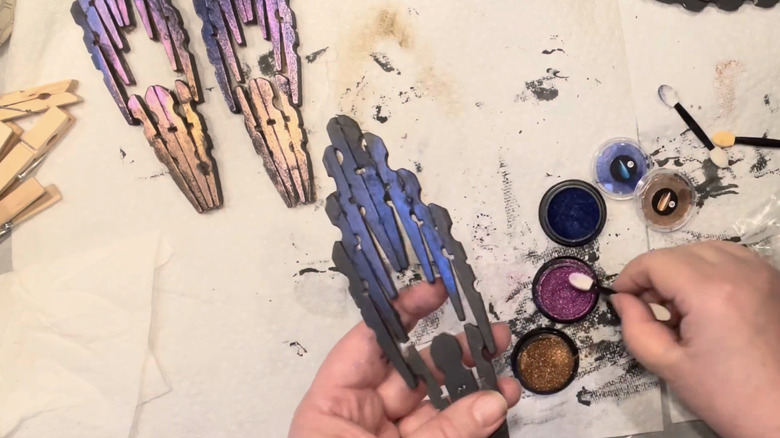 A person paints dragonfly wings made out of clothespins in shimmery colors.