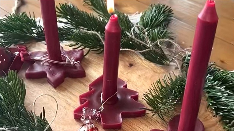 Standing red tapered candles with molded wax bases in holiday shapes