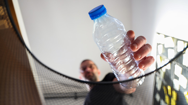 Man holding an empty plastic bottle over a trash bin
