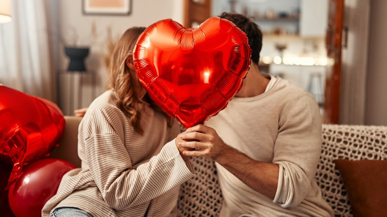 Couple kissing behind a red heart balloon