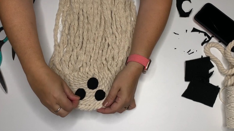 Woman's hands gluing black felt eye over rope ghost