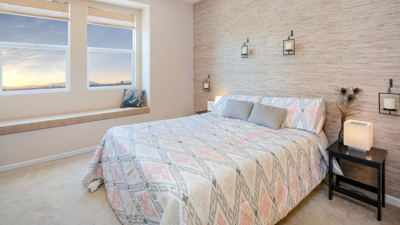 A bedroom with a beige, pink, and light gray color scheme has a grasscloth accent wall.
