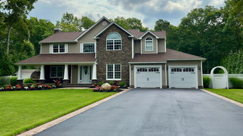 A black asphalt driveway leading up to a two-story home with a neat green lawn