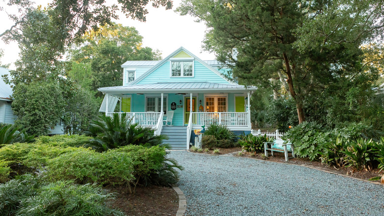 A gray gravel driveway leading to a blue house with a white porch surrounded by trees