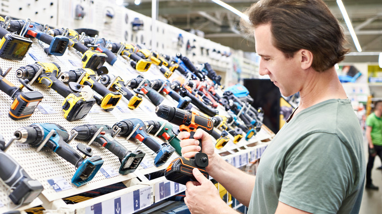 Man examining power drill in hardware store.