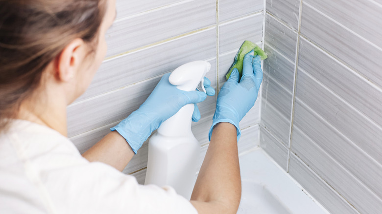 Gloved hands applying grout to ceramic mosaic tiles.