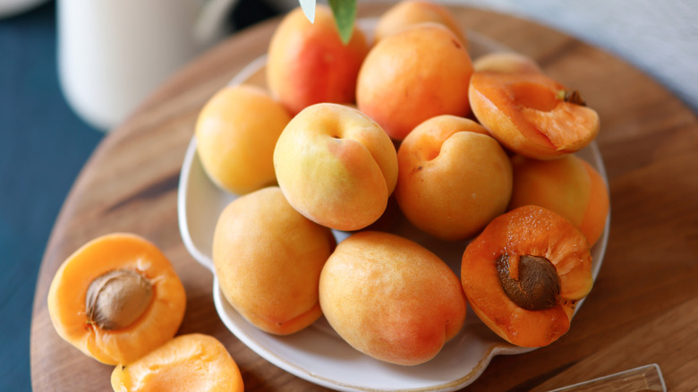 Fresh apricots on a plate with two cut in half on a wood table