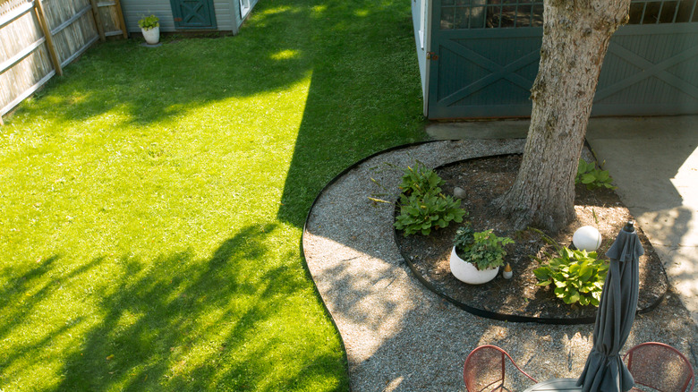 Shady green lawn with curved gravel path and patio set.