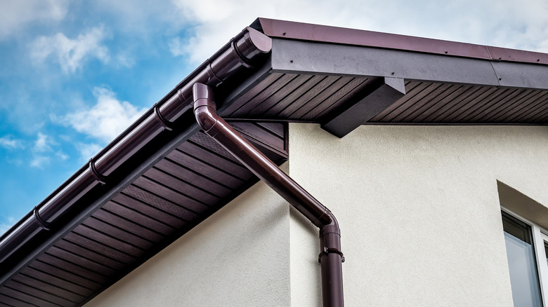A dark metal gutter attached to the roof of a modern home