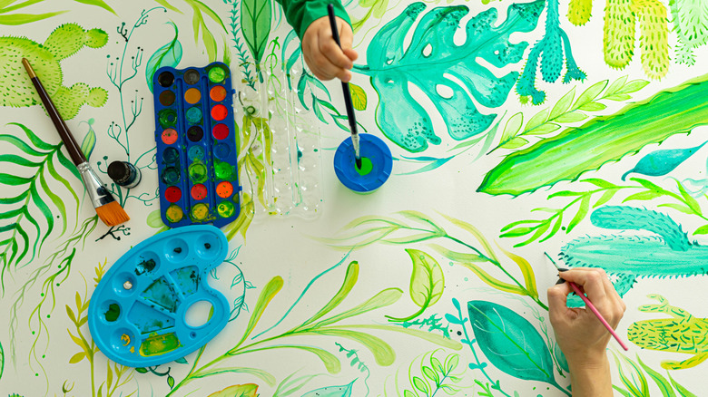 Child and adult hands paint a mural on a surface