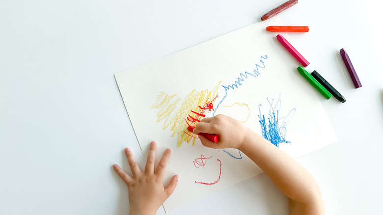 Child draws with crayons on paper on white table top