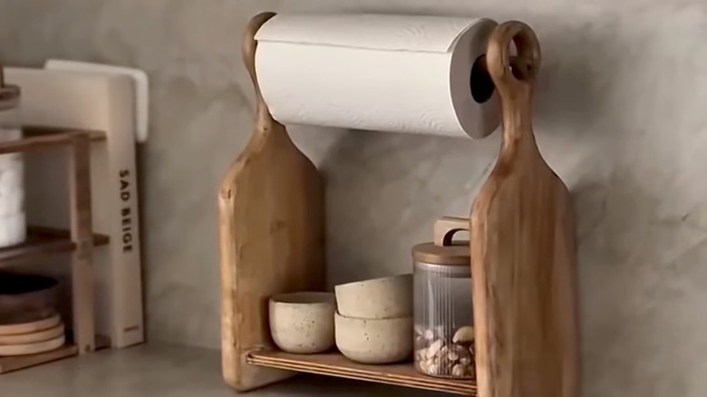 A paper towel dispenser made out of two cutting boards sits on a countertop in a kitchen.