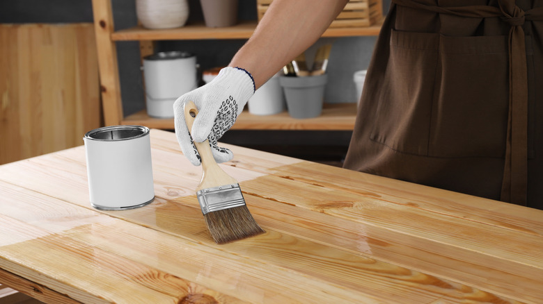 A person using a paint brush to add varnish to the top of a wood table