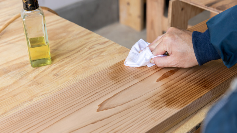 A person's hand applying walnut oil to a piece of wood using a cloth