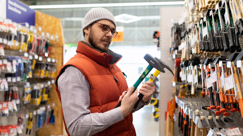 Man considers two hammers at hardware store