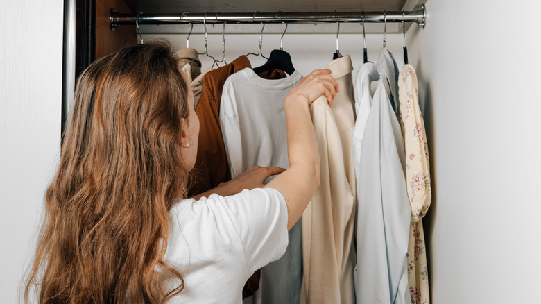 Woman going through clothes hanging in a closet, deciding what to wear
