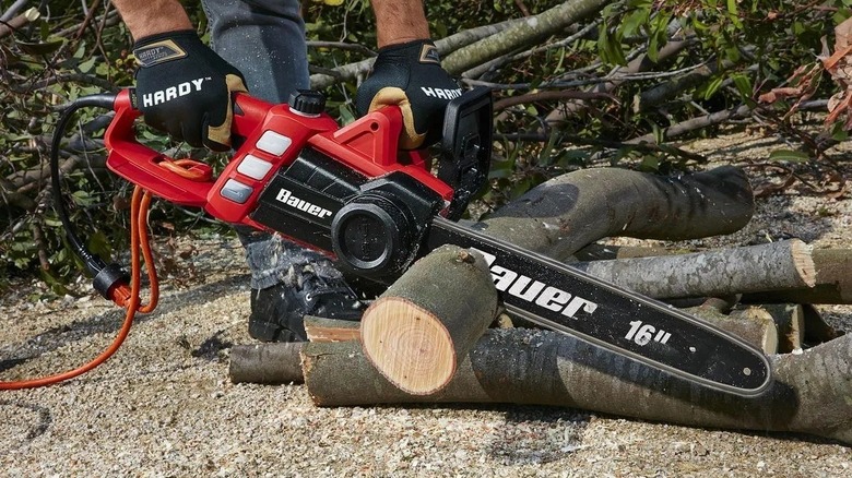 Person cuts through a log on the ground with a Bauer corded chainsaw