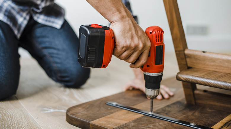 person assembling wood furniture with drill