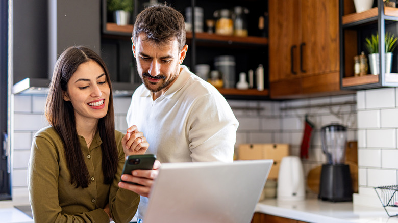 couple looking at phone and computer in kitchen