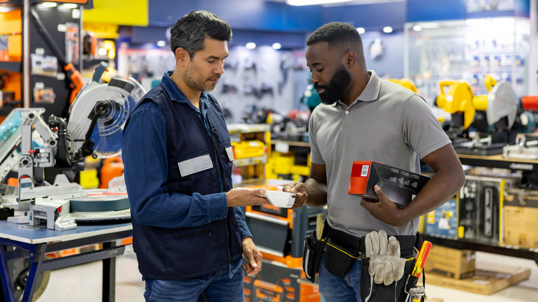 An employee in a hardware store discusses an item with a handyman