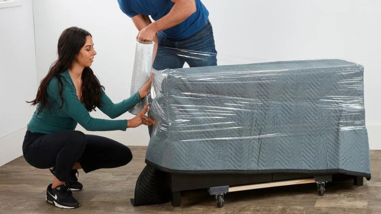 A couple using Franklin's 18 in. x 1,000 ft. High-Performance Stretch Wrap to help protect a piece of furniture