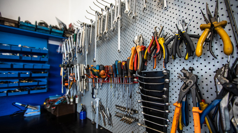 A wall of tools hanging up, including pliers, screwdrivers, and wrenches on a peg board