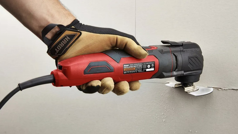 A gloved hand holding the Bauer 3 Amp Variable-Speed Oscillating Multi-Tool while cutting through drywall.