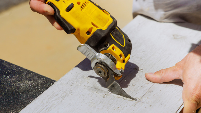 Worker is cutting hole in laminate panel with multitool.