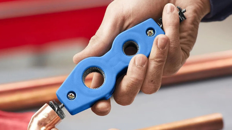 A person using Harbor Freight's 4-in-1 Plumber's Brush to clean copper pipe