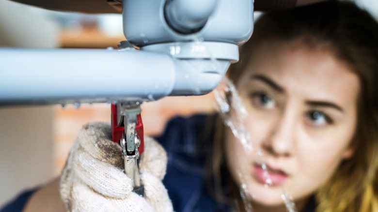 A woman fixing a leaky sink pipe